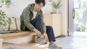 長時間歩いた後、玄関で靴ひもを緩めて足を休める男性
